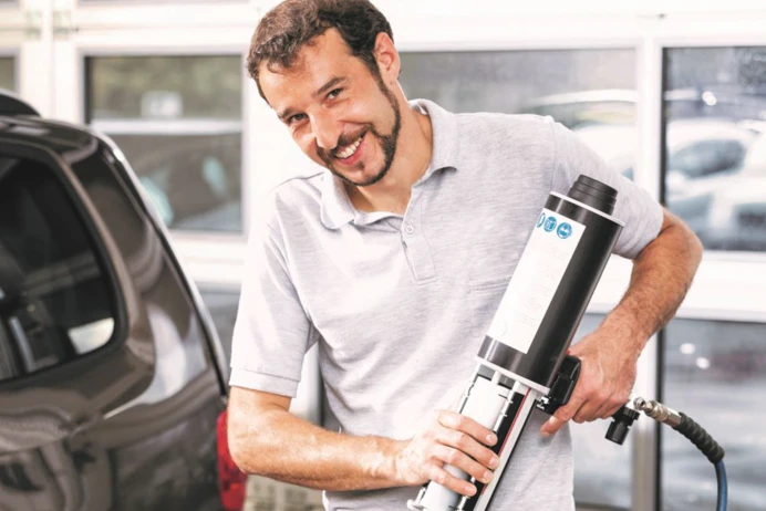 Man using tool on a car looking at camera